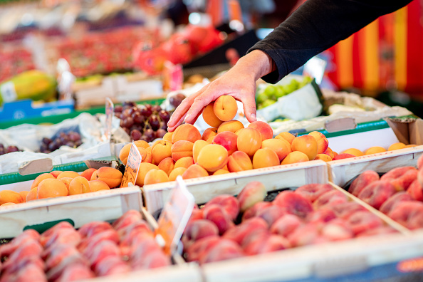 A vendor reaches into a crate of apricots at a fruit and vegetable stand