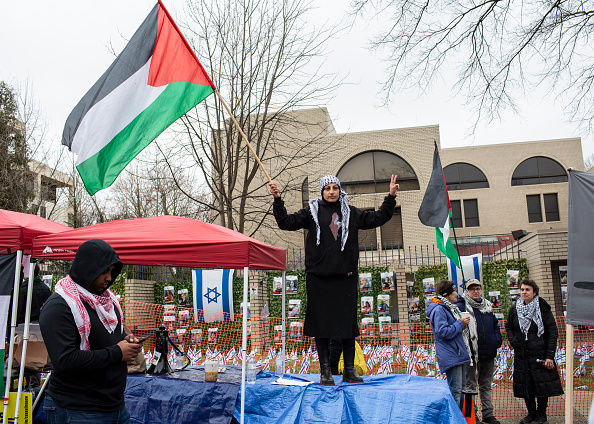 A demonstrator holding palestinian flags gathers outside of the Israeli Embassy