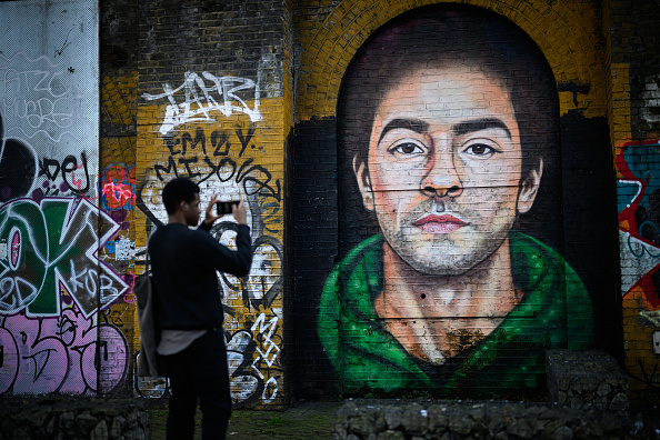 A man takes a photo of a mural of Luigi Mangione