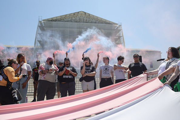 Supporters of gender-affirming care hold colored smoke devices during a rally outside of the Supreme Court