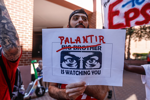 Demonstrators carry placards and portraits demanding the shutdown of Palantir Technologies