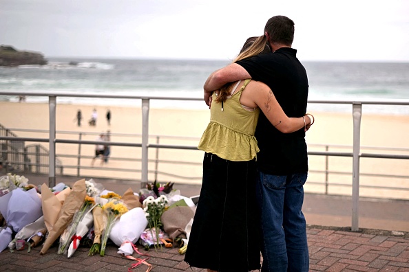 Mourners embrace near tributes piled together in memory of the victims of the shooting at Bondi Beach, in Sydney