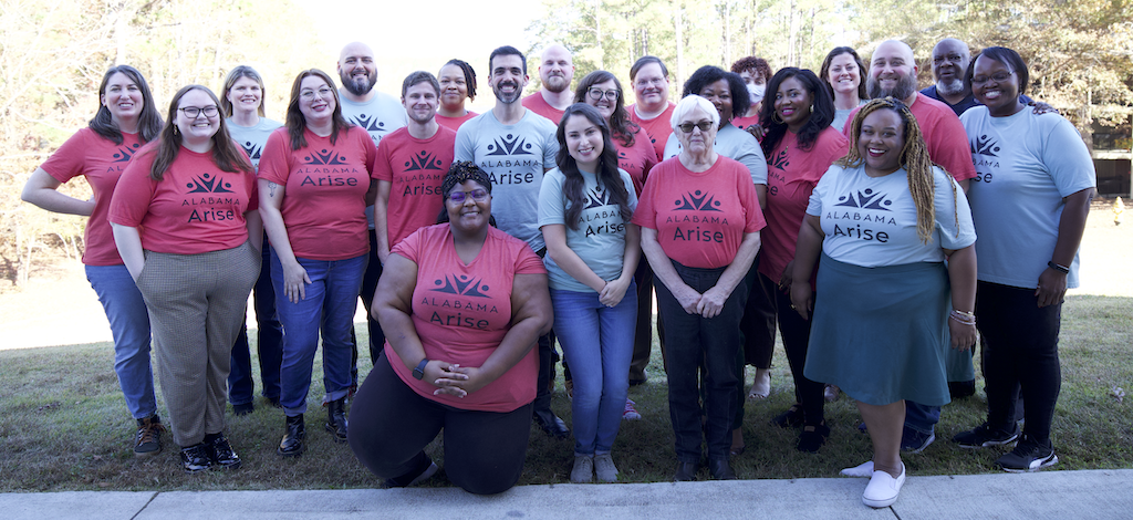 Twenty three people stand outside in matching red and green t-shirts