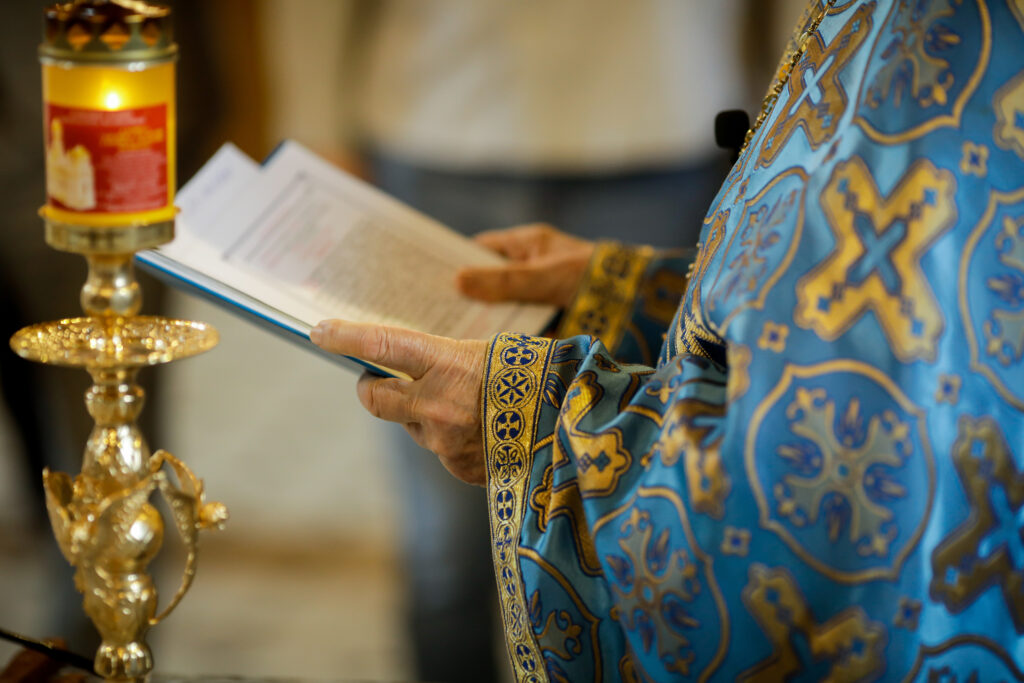 Hands of priest holding book near candle
